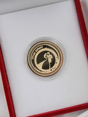 Zlatni zlatnik sa romantičnim prikazom mladenaca u zagrljaju i natpisom „Срећно венчање“. Smešten u crvenu kutiju sa belom postavom. Savršen poklon za venčanje – spoj elegancije, ljubavi i večnog sećanja.