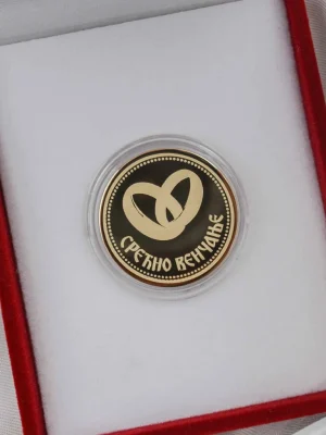 Zlatni zlatnik sa simbolom venčanih prstenova i natpisom „Срећно венчање“, smešten u crvenu kutiju sa belom postavom. Elegantno i trajno rešenje kao poklon za mladence – uspomena na večnu ljubav.